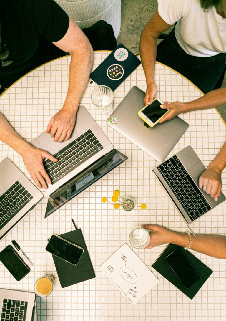 Top view of a team collaborating with laptops, phones, and notes in a modern office.